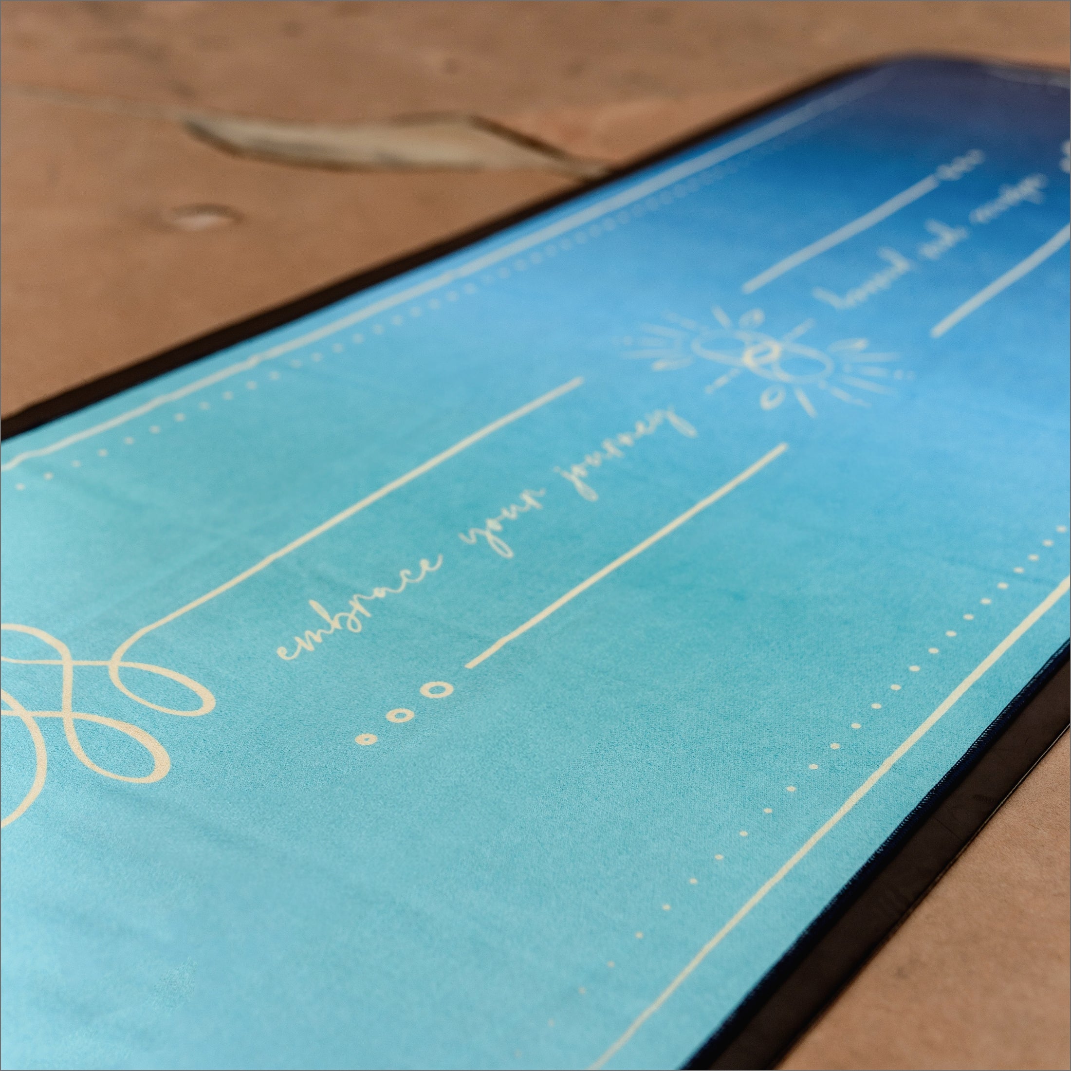 Close up of Blue Ananta Unalome Yoga Hot Yoga Towel made from eco friendly materials and 44% more silicone grip on the back. simple design with white lettering
