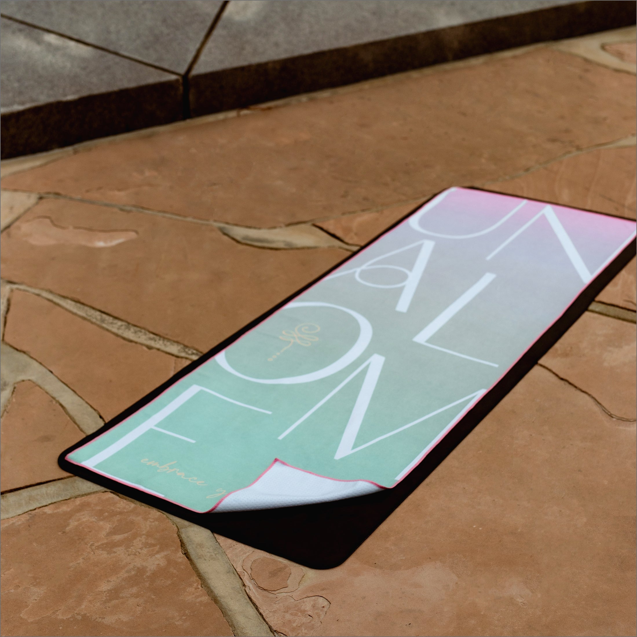 Non slip yoga towel grip with 44% more silicone coverage. Mint and light pink colors. White lettering of 'unalome' with logo and tagline 'embrace your journey'