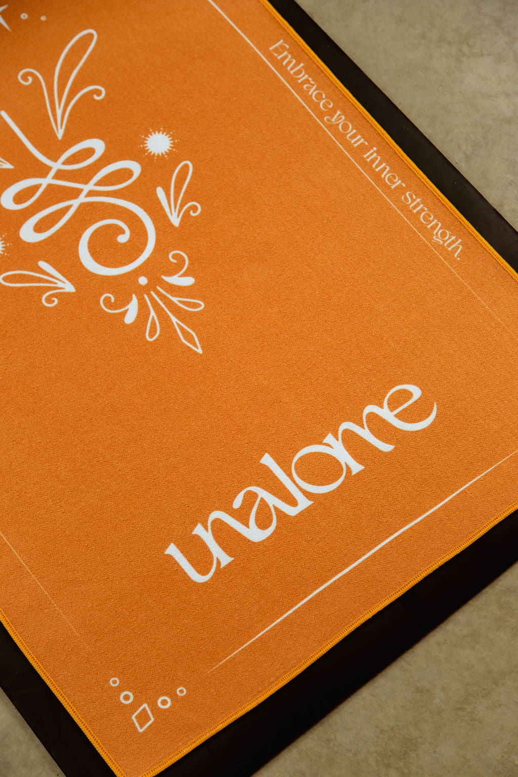 Unalome Yoga logo on Gaia towel – eco-conscious hot yoga towel with 44% more silicone grip; orange background with white symbols