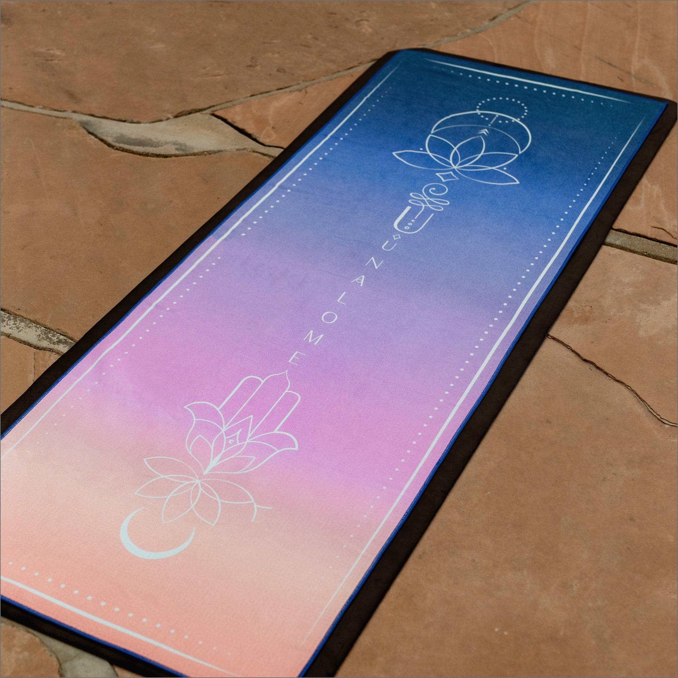 Unalome Sunset towel placed on yoga mat outside at a park — vibrant gradient colors and non-slip grip and eco friendly materials