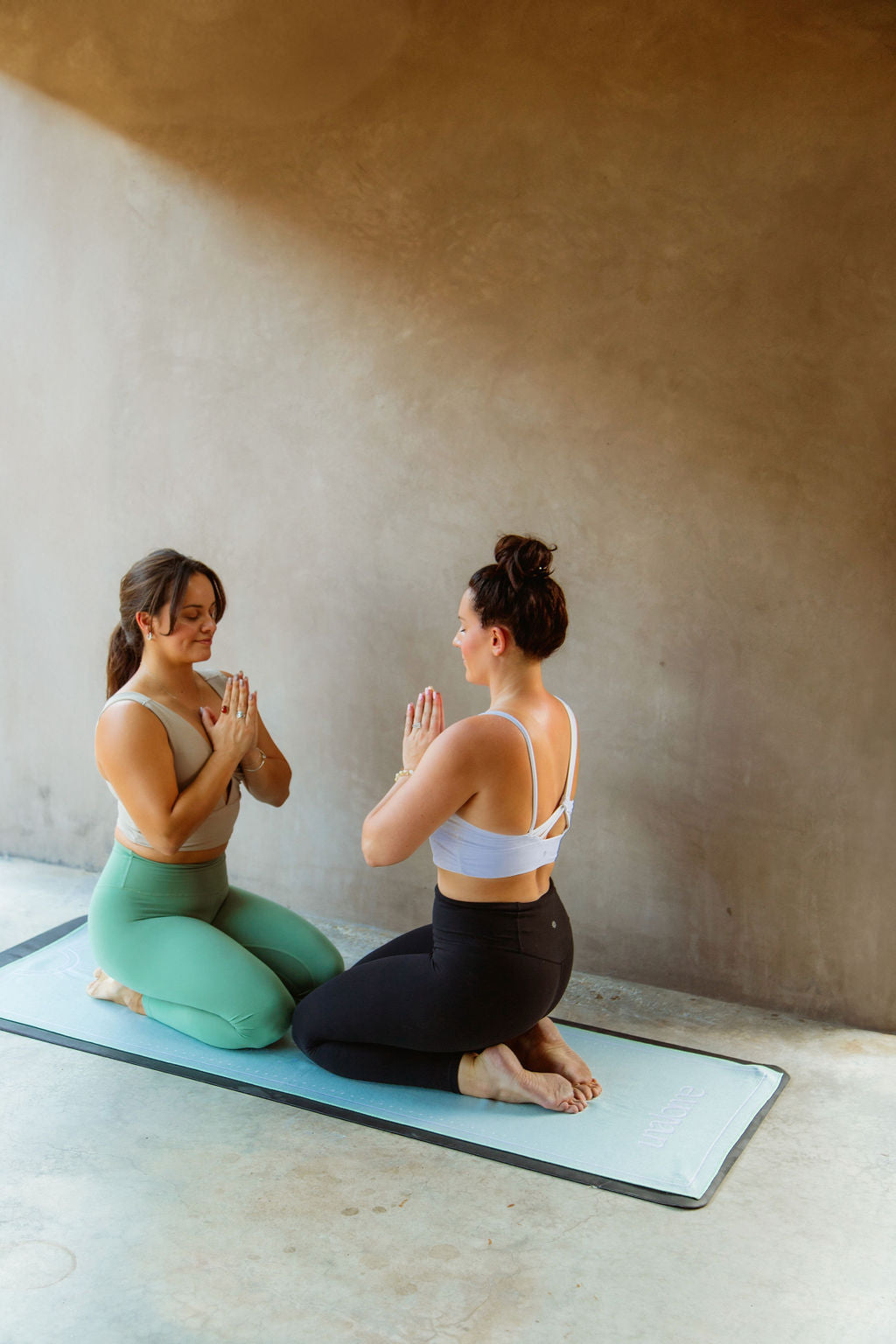 Two women practicing yoga on a mat and green non slip yoga towel with luxurious microfiber blend