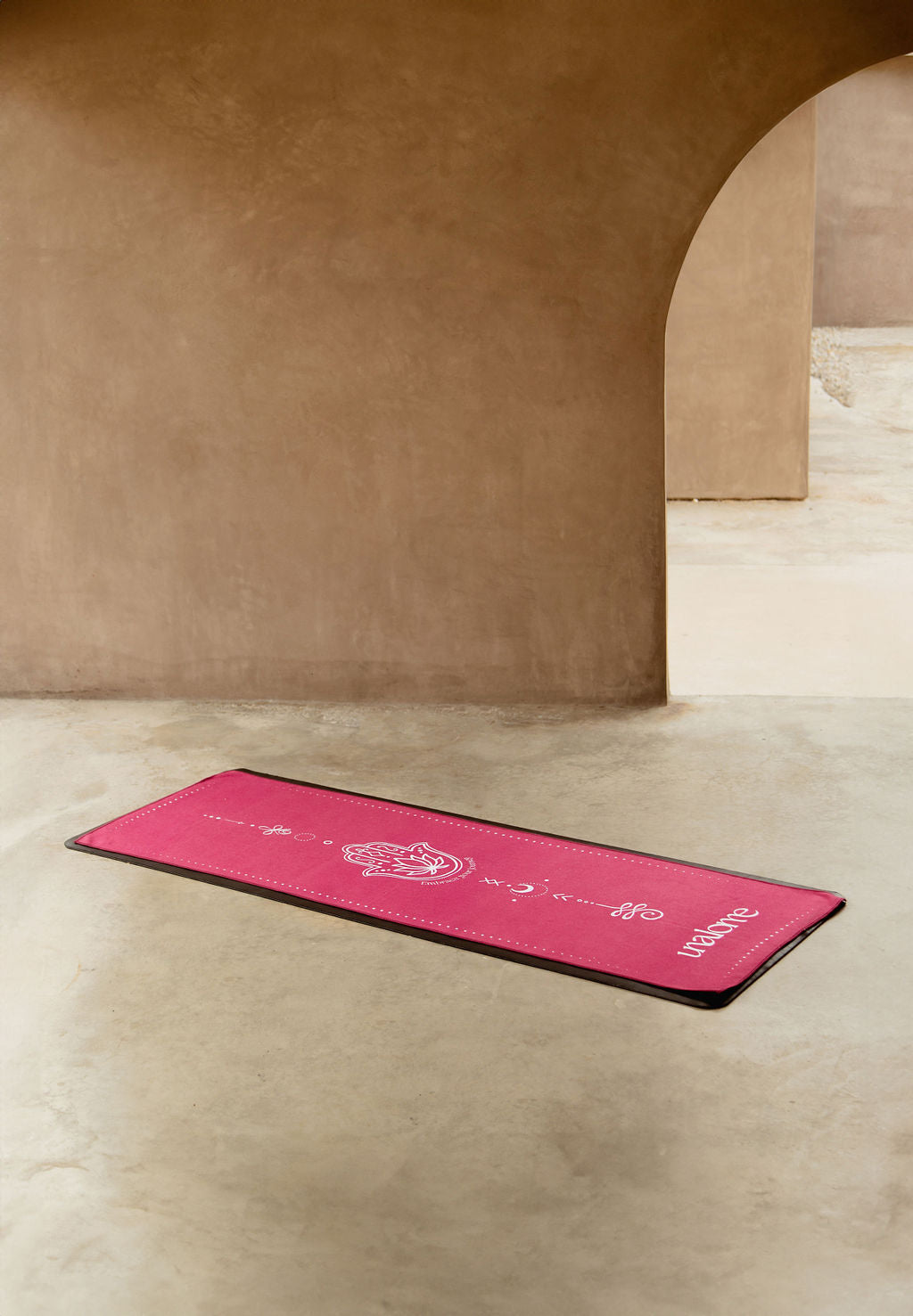 Deep pink non slip and luxurious microfiber blend hot yoga towel on top of black yoga mat. White symbols throughout