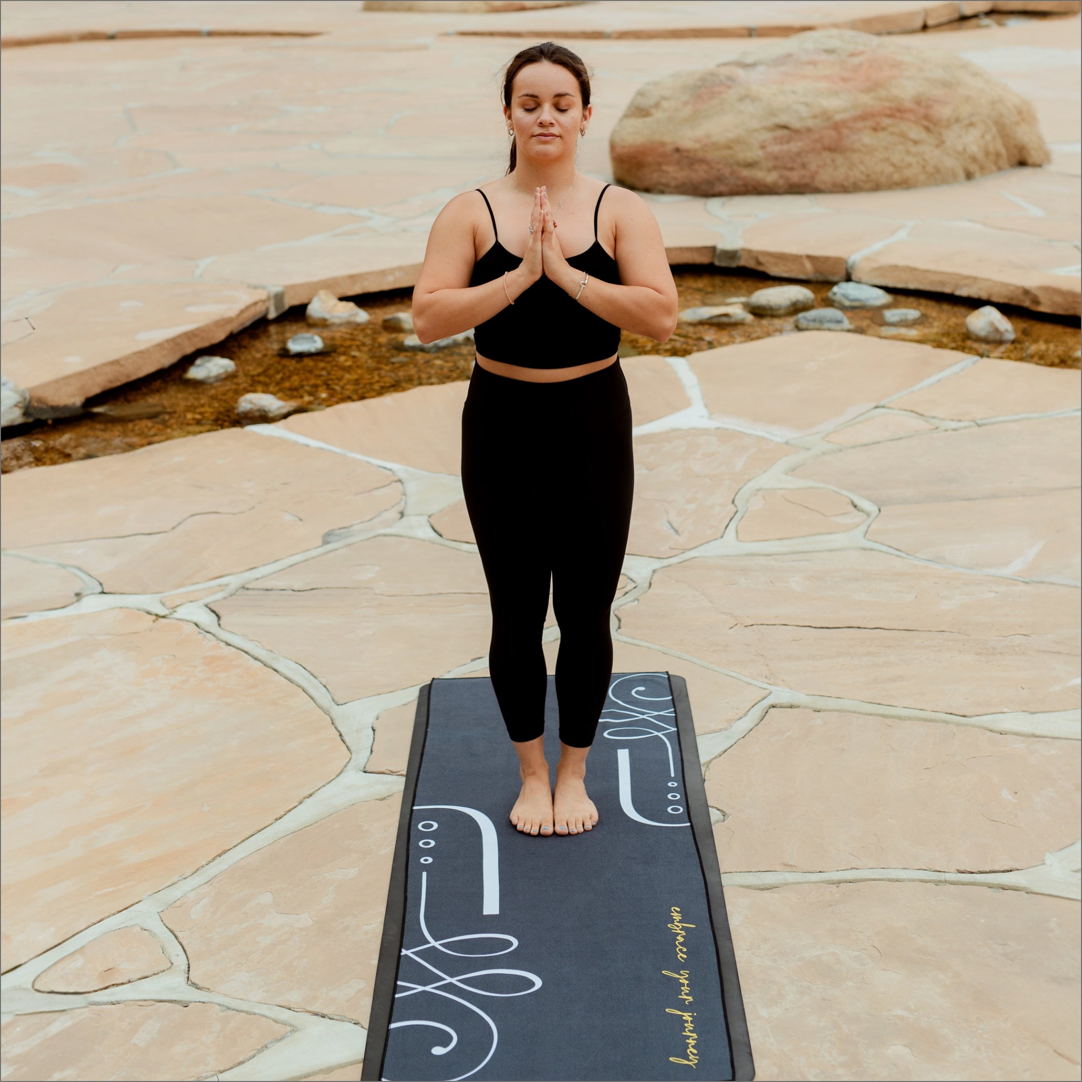yogi on black yoga towel in park setting. minimal designs with white lettering and unalome logo